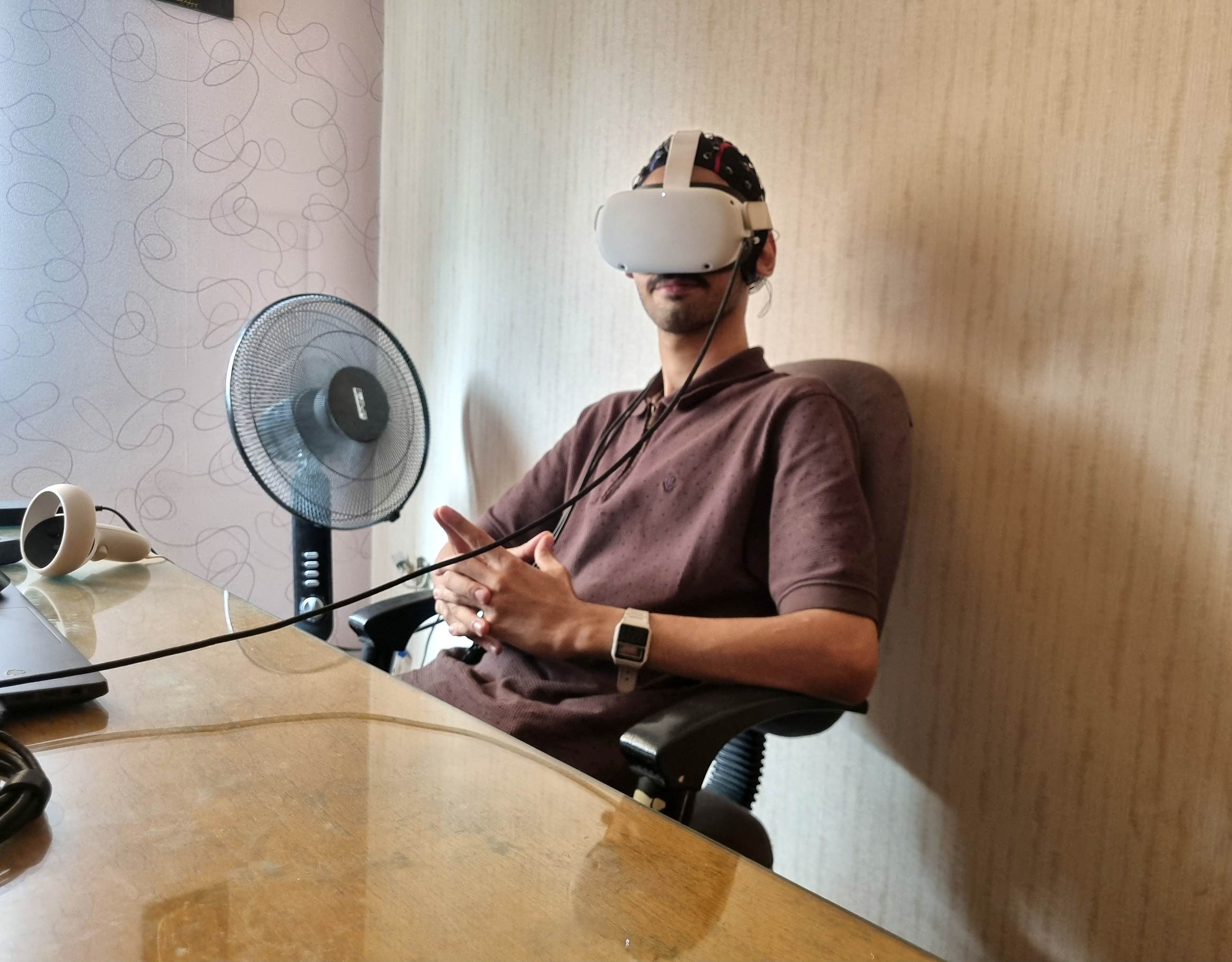 Kiarash seated at a desk wearing an EEG cap and VR headset