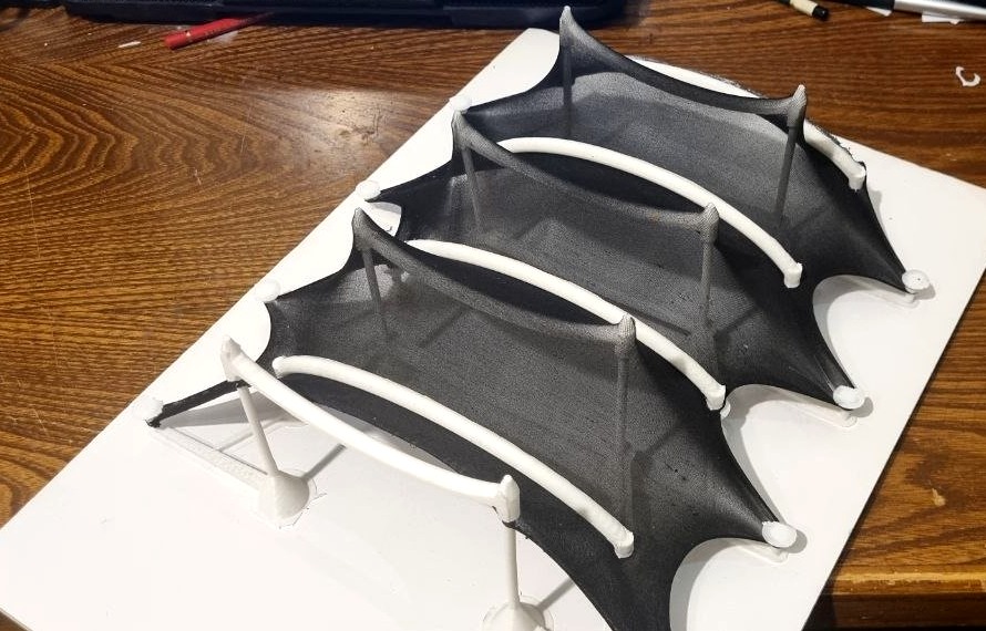 Physical roof study model with dark membrane stretched between its peaks and curved members