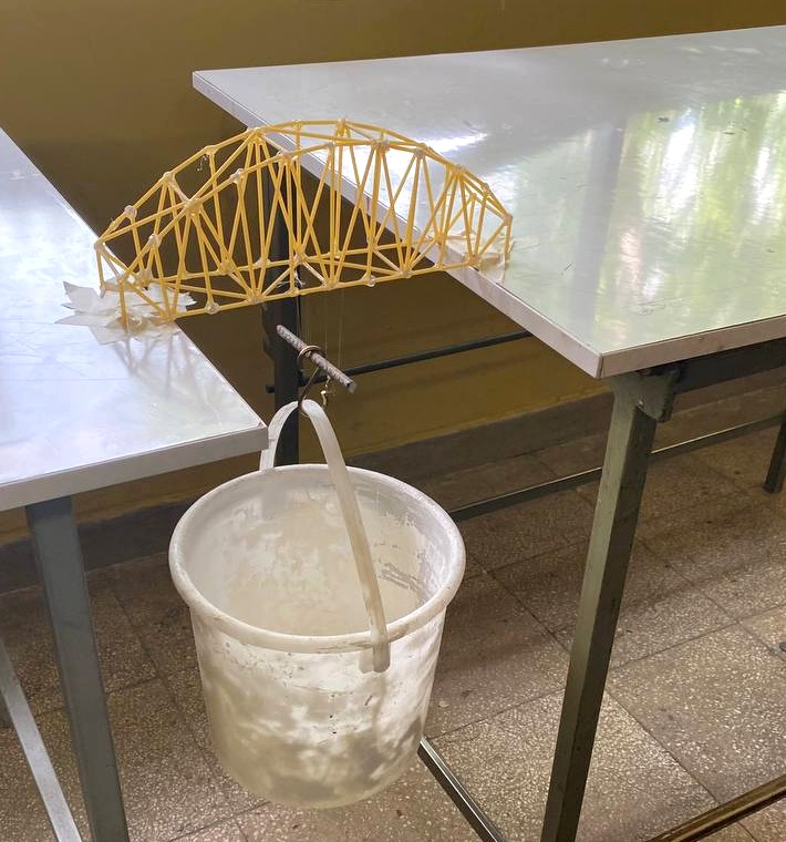 Group-built yellow truss model spanning two tables with a bucket suspended beneath the deck