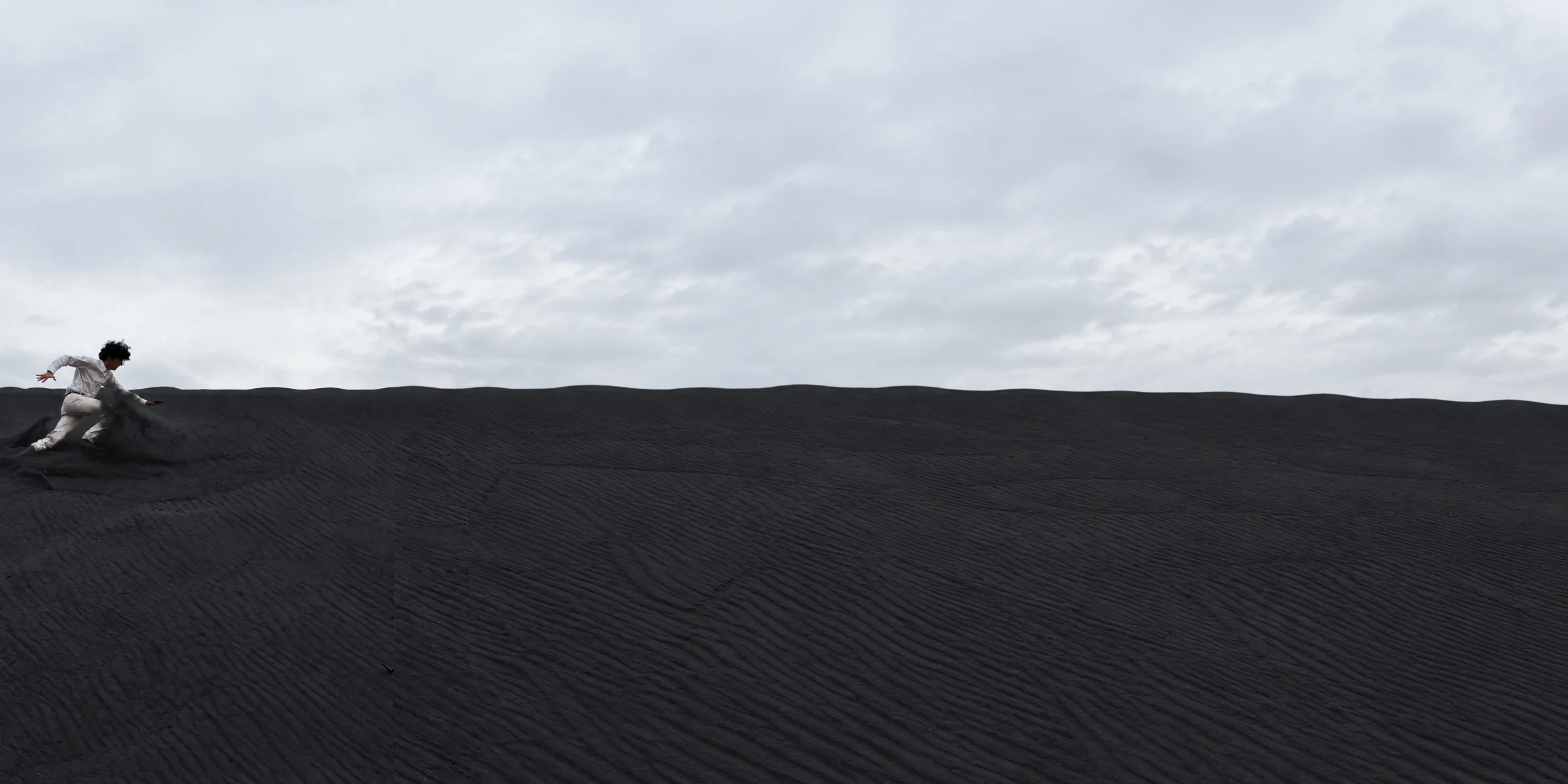 Kiarash on a wide black-sand landscape beneath a cloudy sky